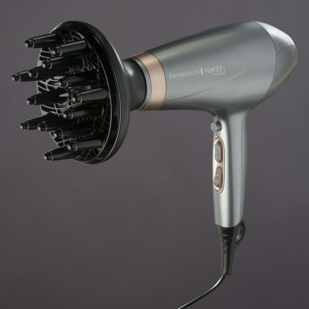 Ein grauer Haartrockner mit aufgesetztem schwarzem Diffusor. Goldakzente und schwarzes Kabel.