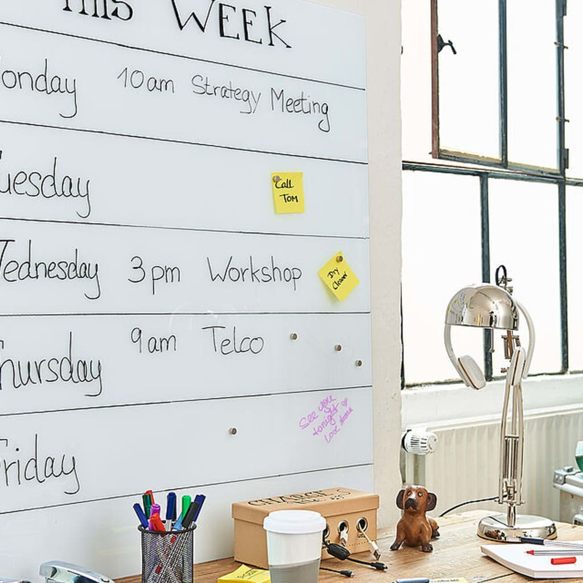 Eine Whiteboard mit Wochenplan, Haftnotizen, Stiften und einer Hundefigur auf einem Schreibtisch.