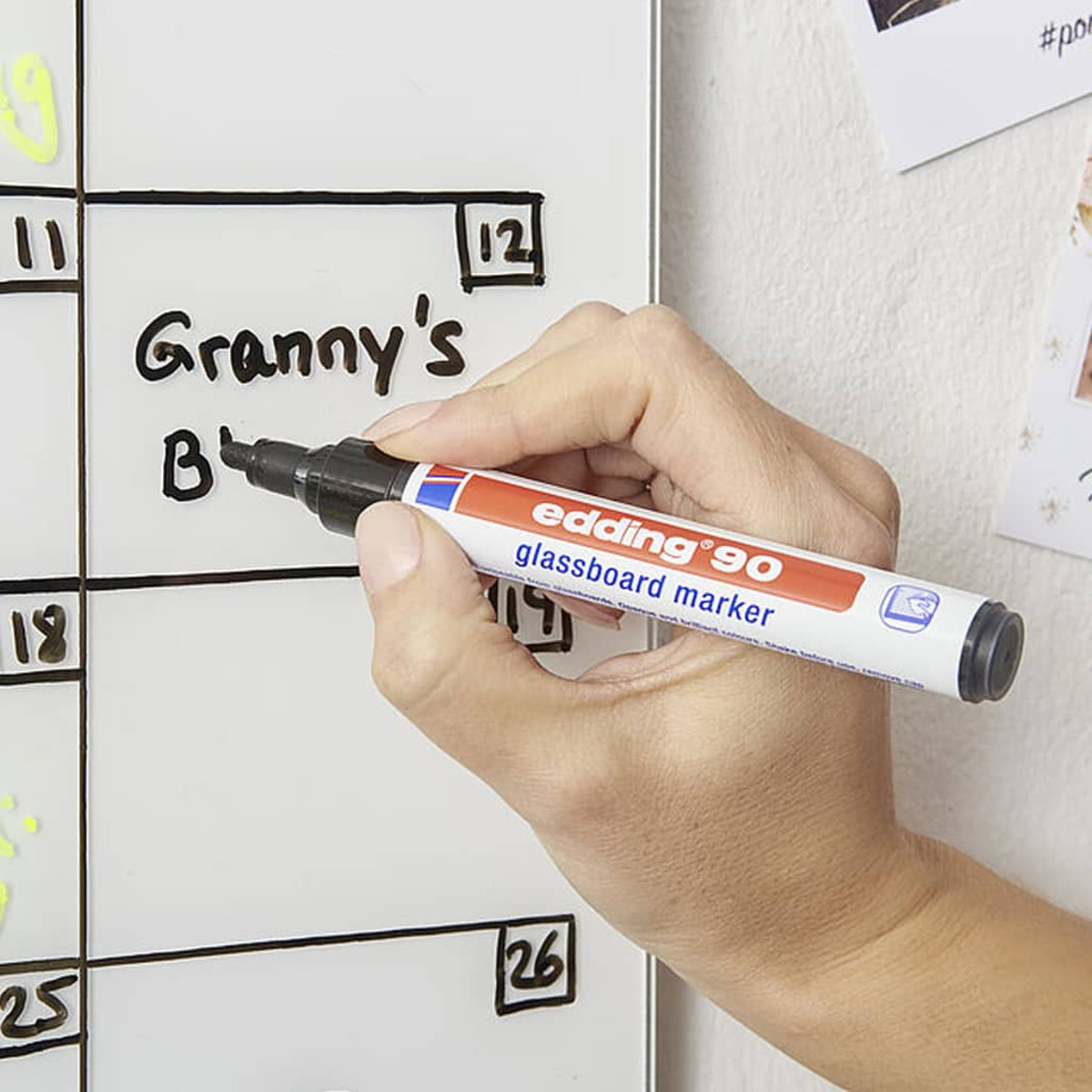 Eine Hand schreibt auf einem Whiteboard-Kalender. Der Marker ist schwarz und trägt die Aufschrift "edding 90".