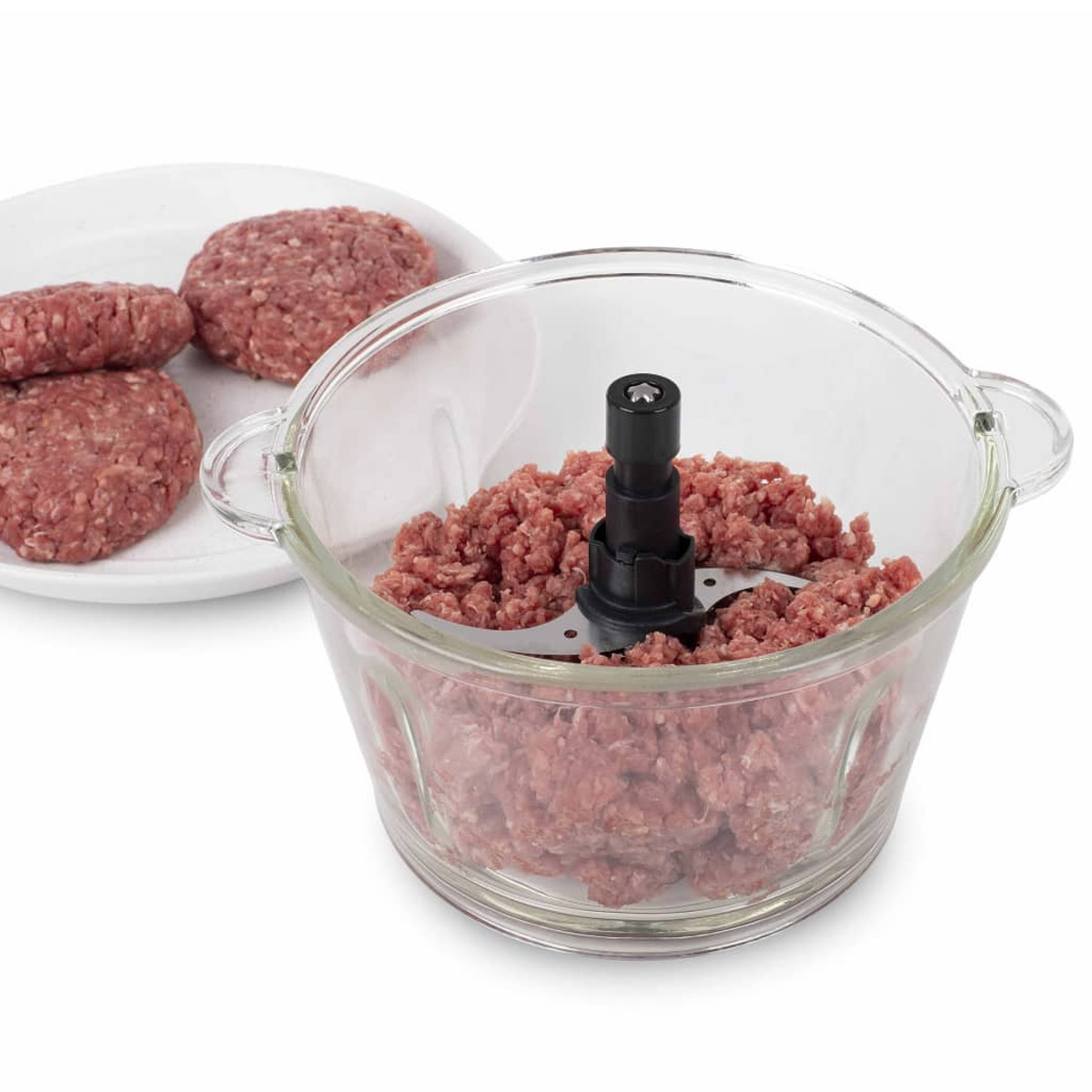 Glasschüssel mit Hackfleisch und Teller mit Buletten auf weißer Oberfläche.