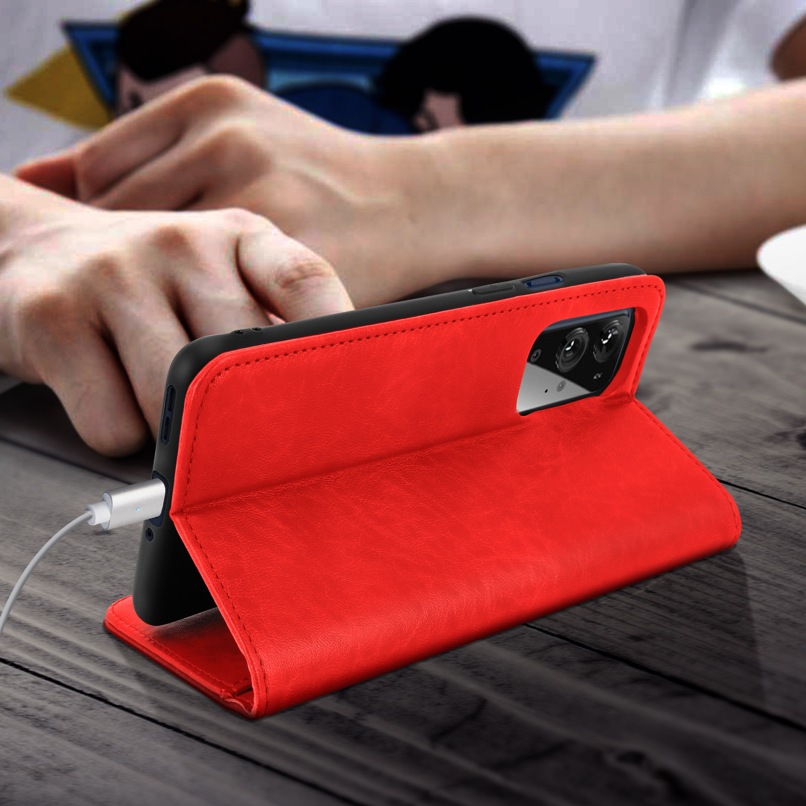Rote Handyhülle, offen auf einem Holztisch. Ein Ladekabel ist eingesteckt. Das Telefon ist drin.