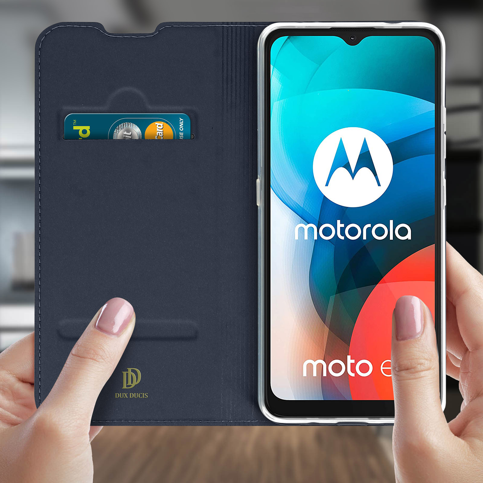 Telefono in custodia blu tenuto in mano. Mostra il logo Motorola e Moto E, e una carta.