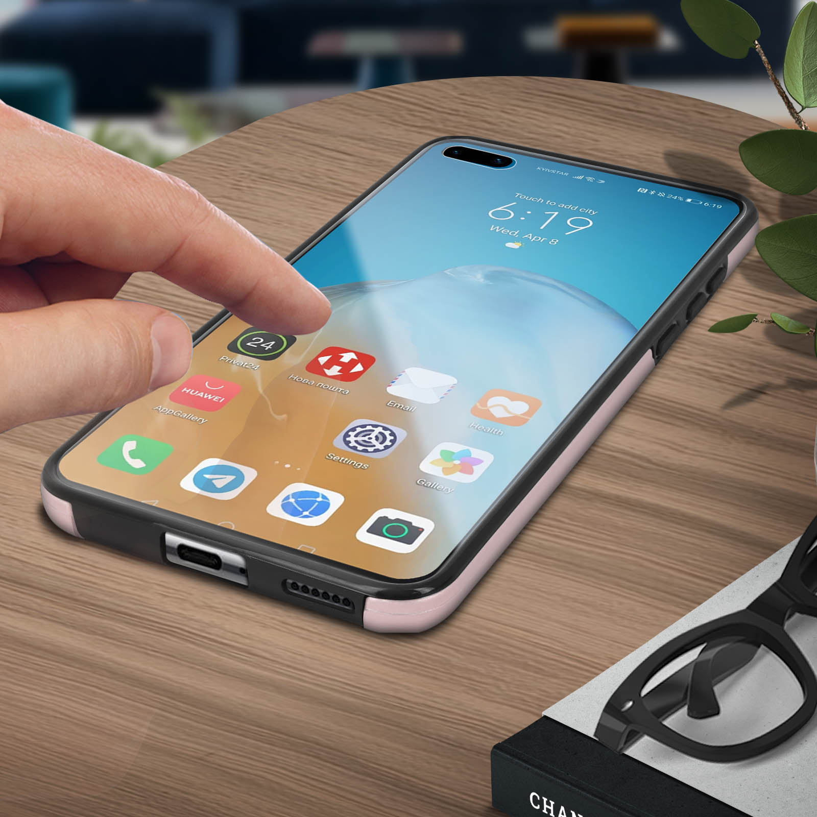 Hand raakt een telefoon aan op een tafel. Apps weergegeven. Plant en bril zichtbaar.