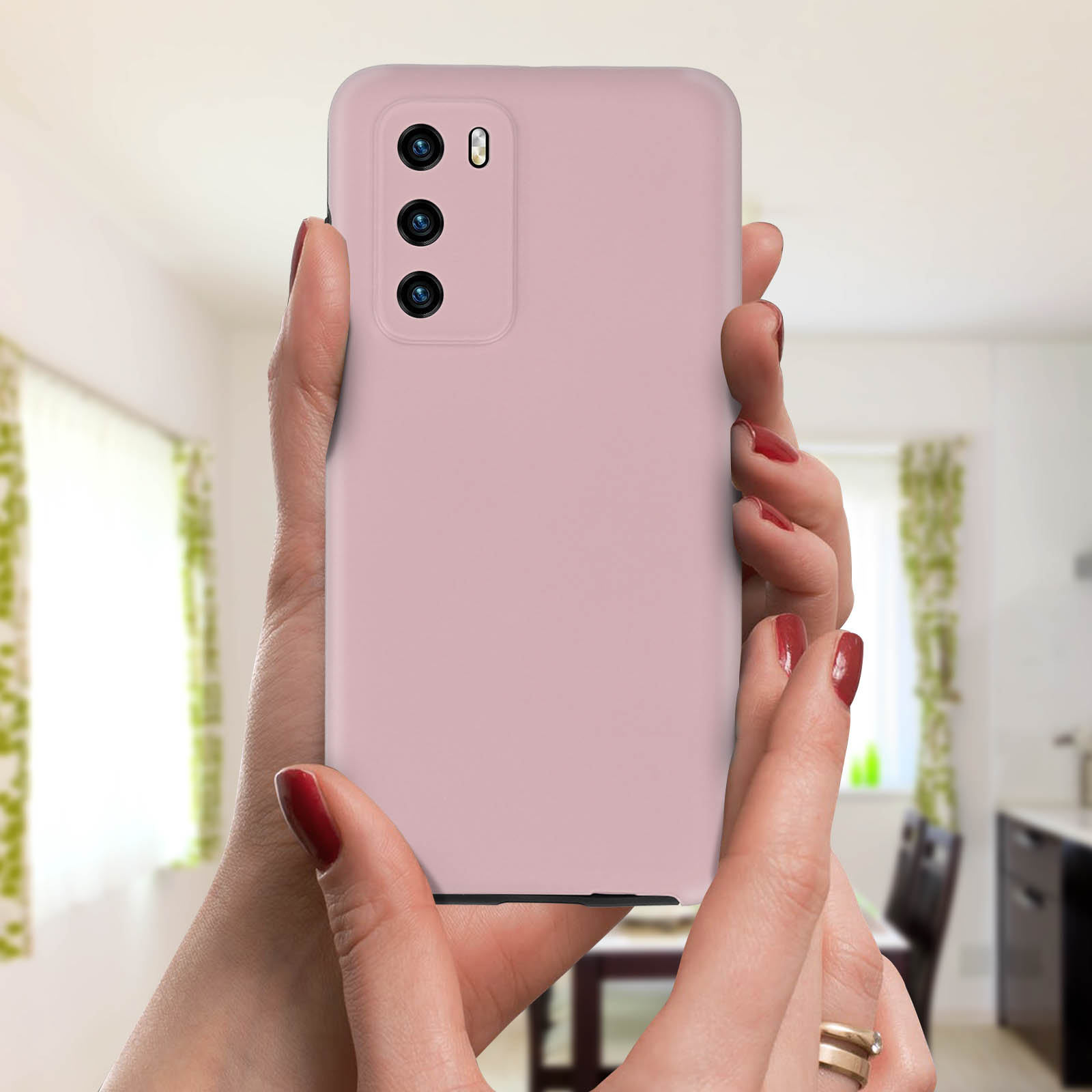 Vrouw houdt een roze telefoon vast. Drievoudige camera's zijn zichtbaar. Achtergrond: keuken.