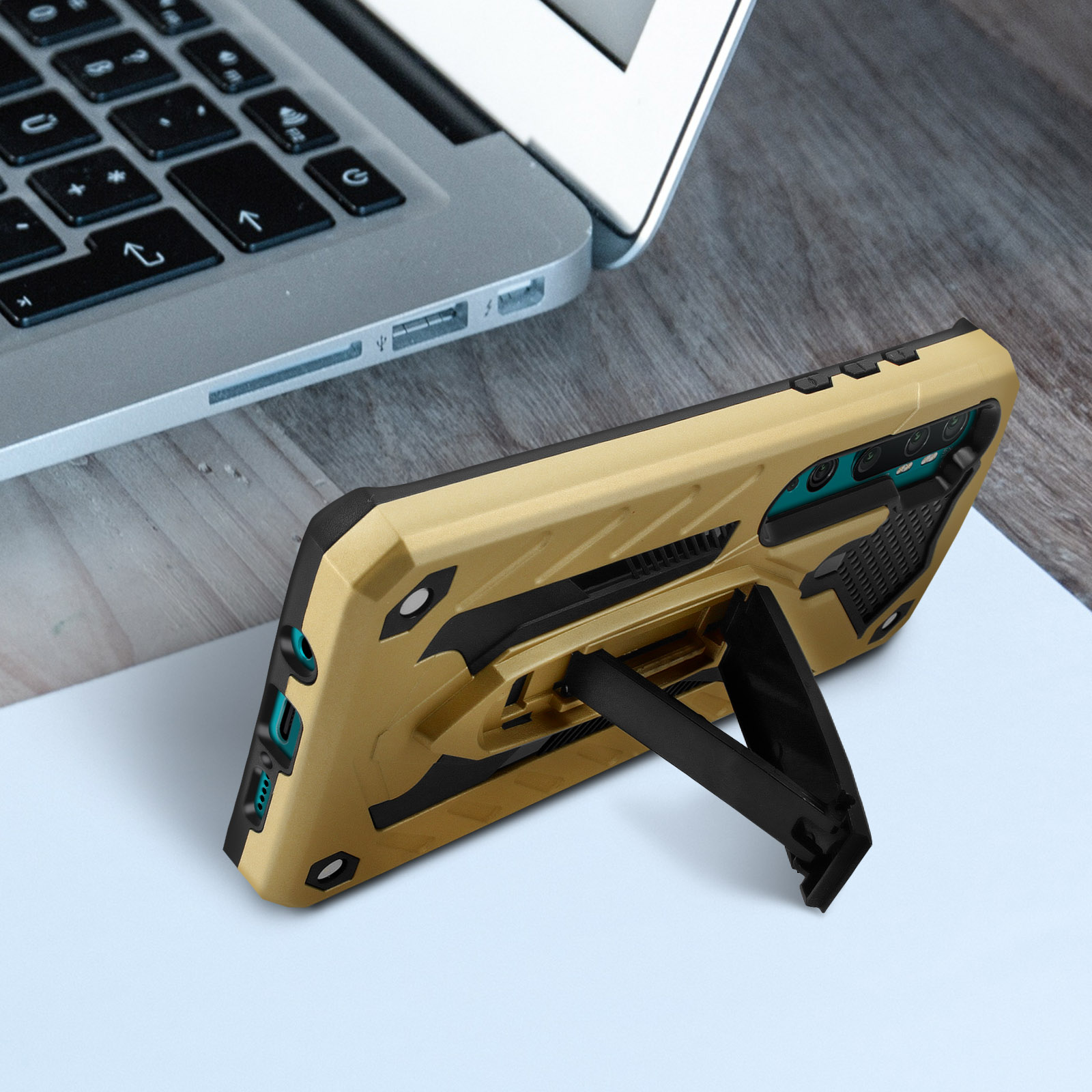 Custodia per telefono dorata con supporto, su un tavolo di legno con un laptop.