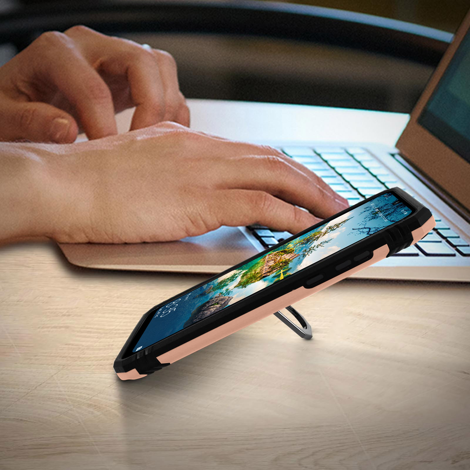Telefon in Hülle auf Tisch. Hände tippen im Hintergrund auf Laptop-Tastatur.