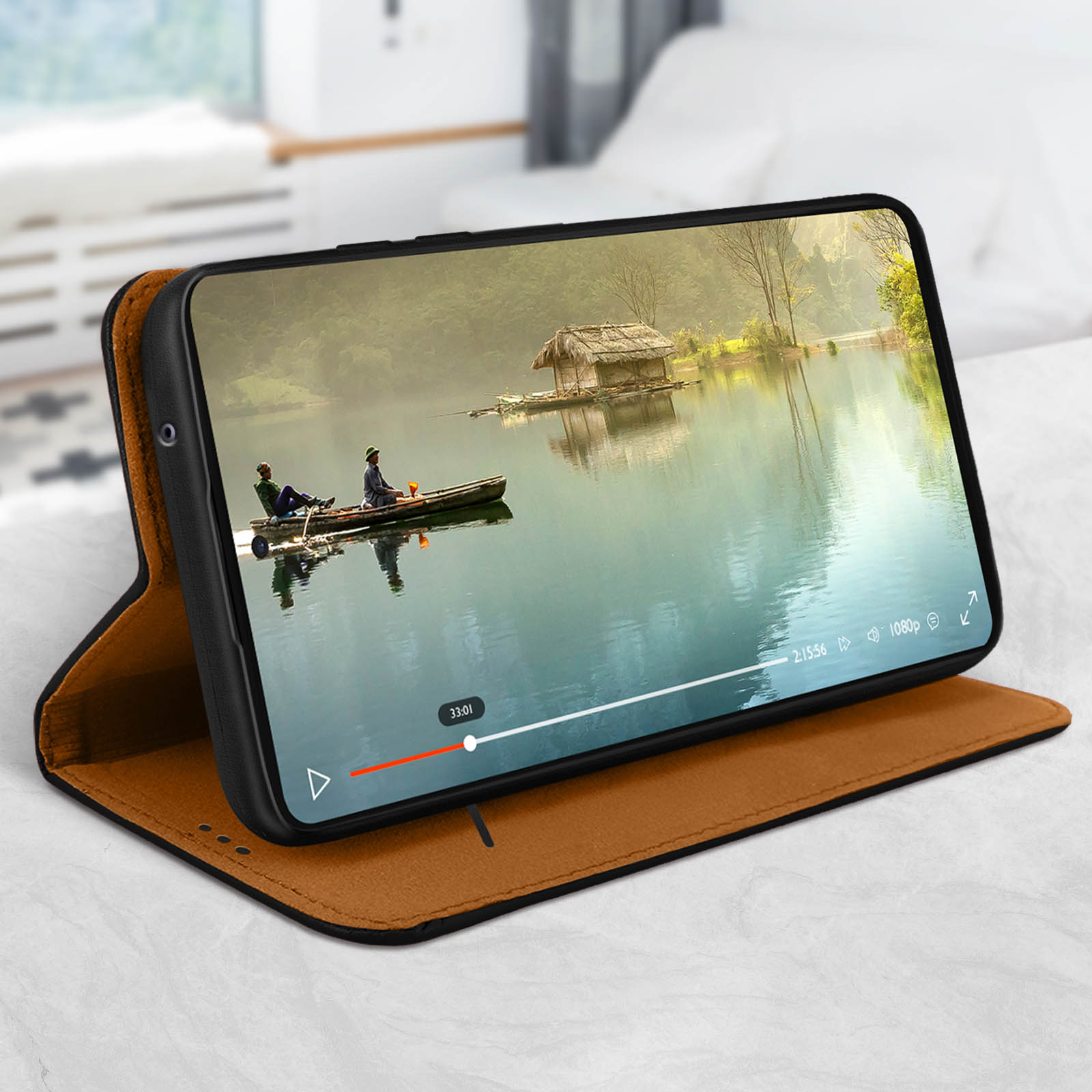 Telefono in una custodia marrone che mostra un video di una barca su un lago. Un letto è sullo sfondo.