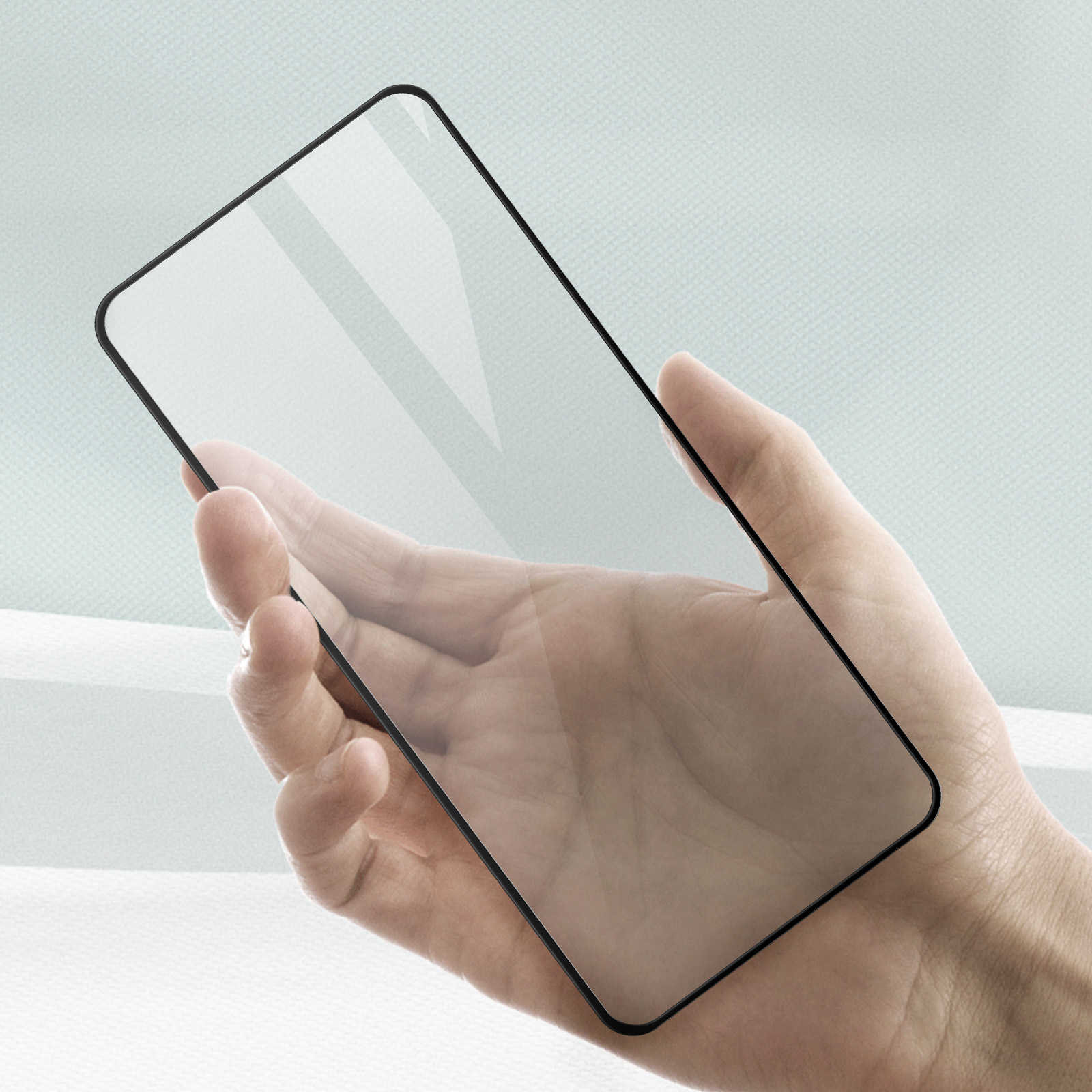 Hand hält einen Glas-Displayschutz mit schwarzen Rändern vor hellblauem Hintergrund.