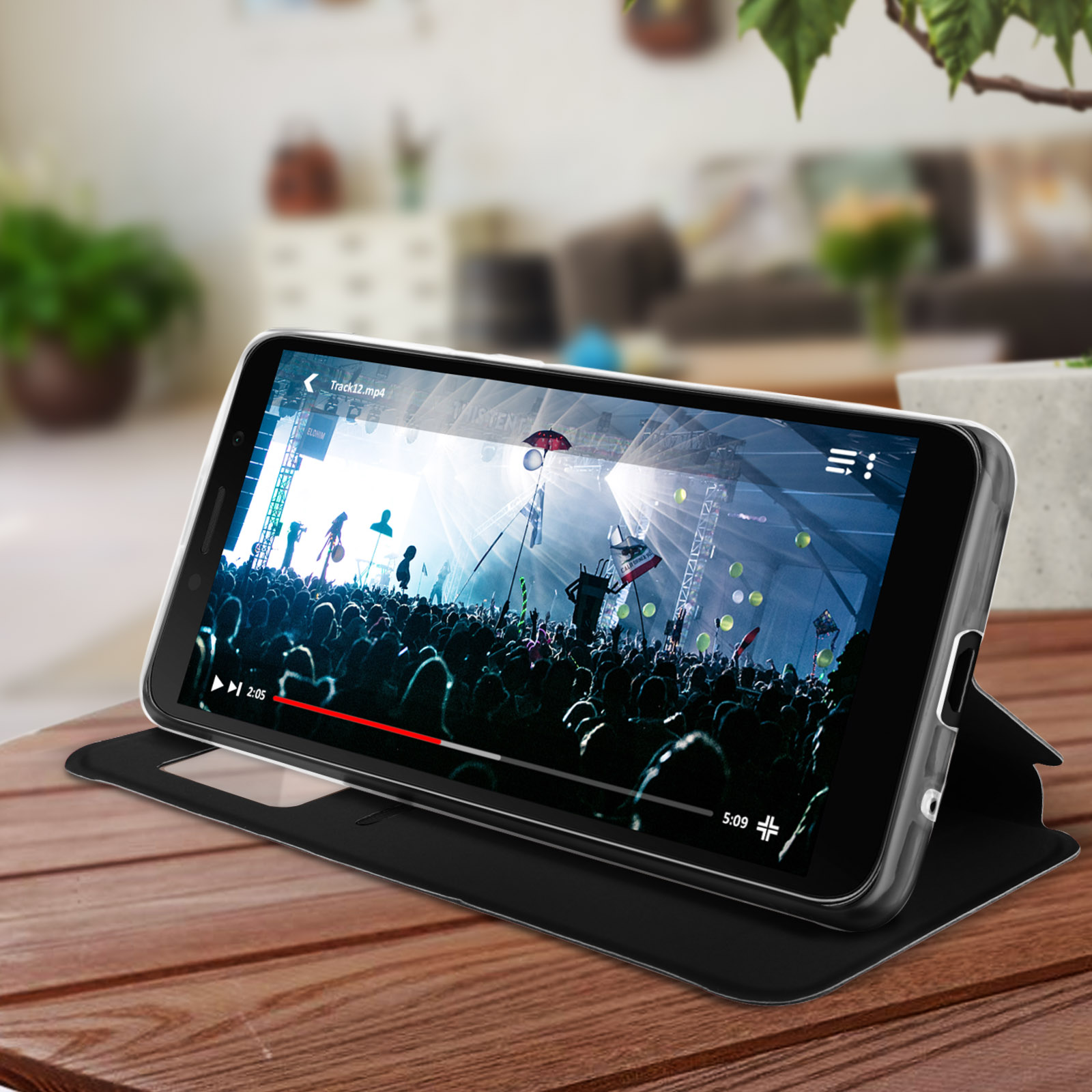 Un telefono con una custodia nera è su un tavolo di legno e riproduce un video di un concerto.