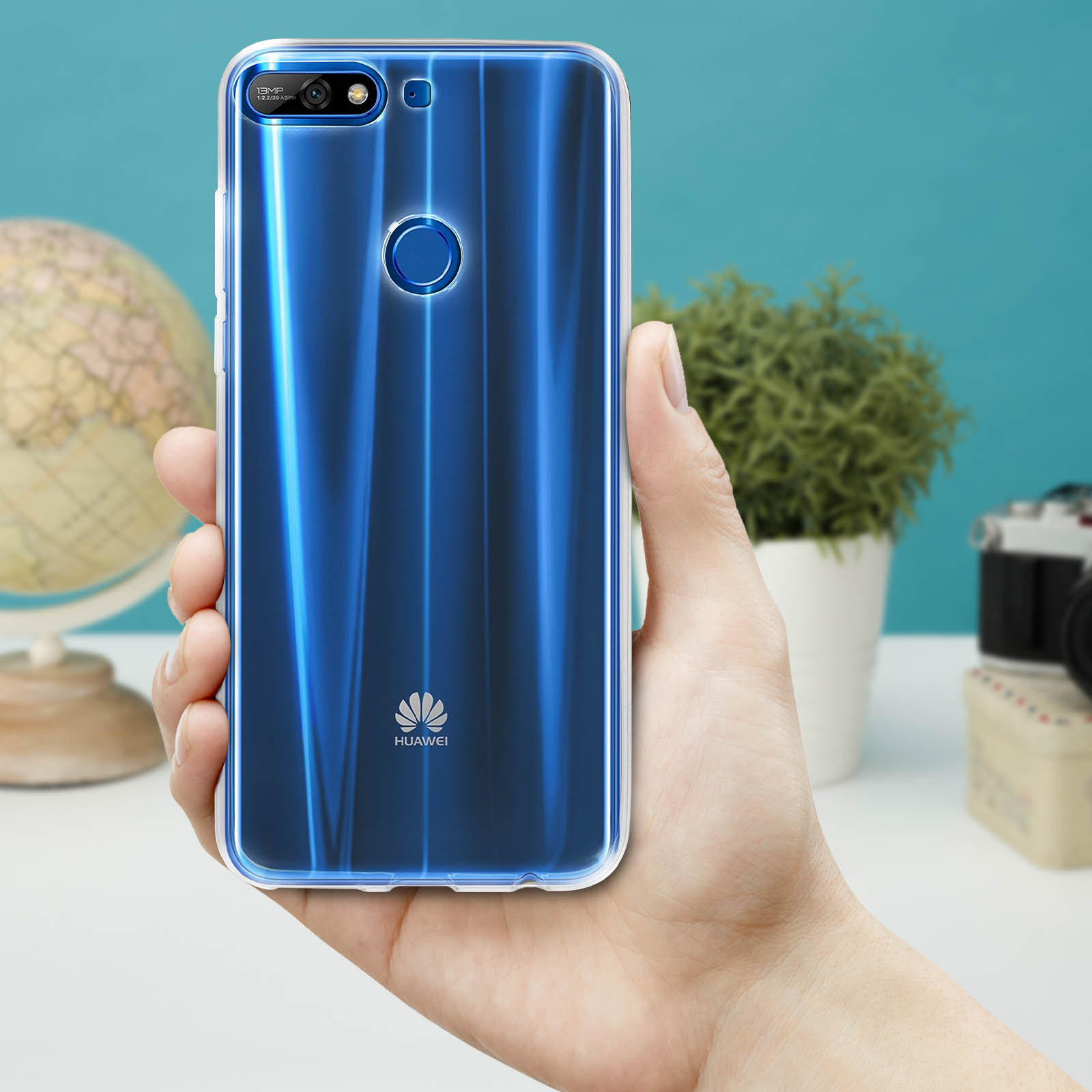 Una mano che tiene un telefono con la parte posteriore blu brillante, accanto a una pianta e una fotocamera.