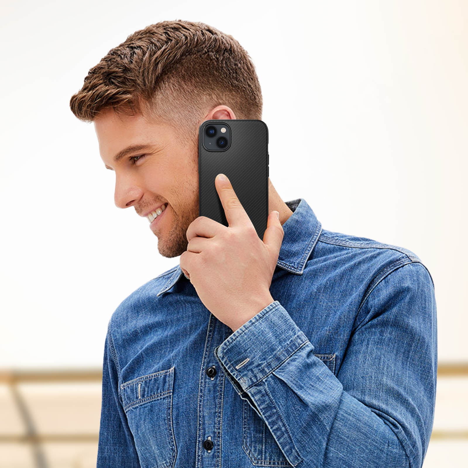 Ein lächelnder Mann hält ein schwarzes Telefon an sein Ohr, trägt ein Jeanshemd.