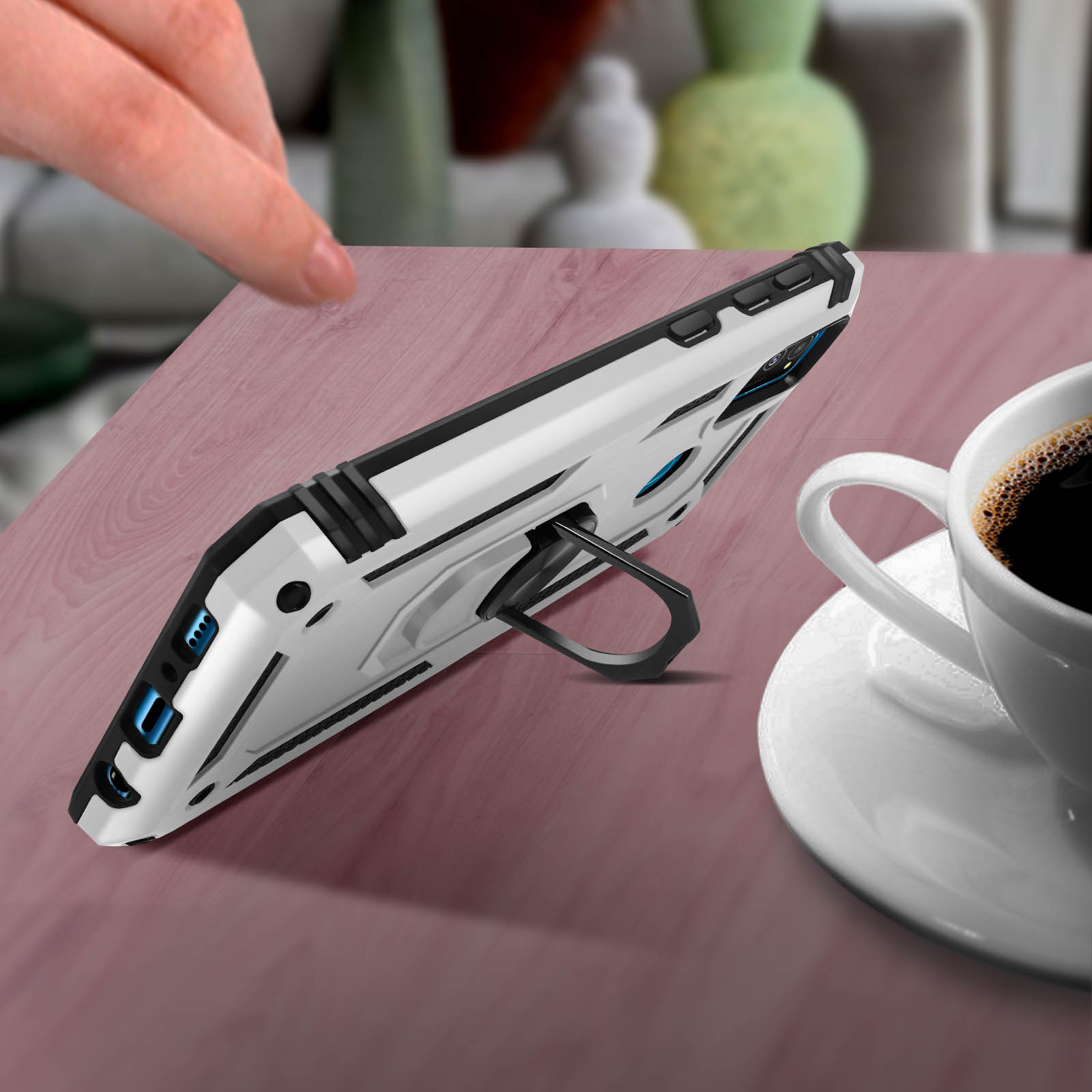 Custodia bianca per telefono con cavalletto, angolata su un tavolo di legno. Tazza di caffè sullo sfondo.