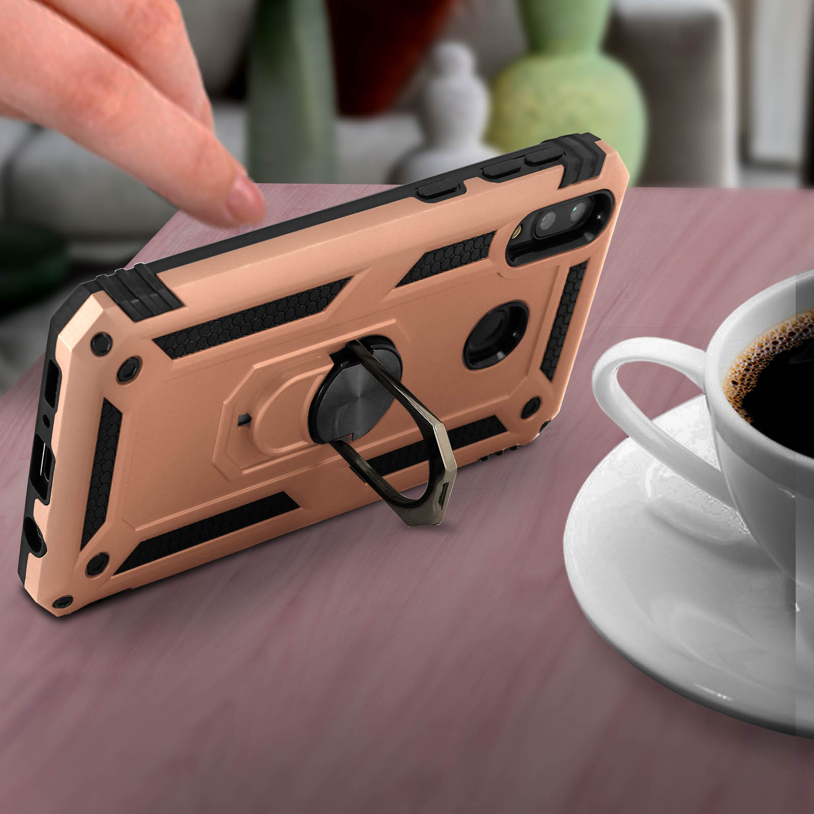 Handy-Hülle mit Ringständer auf Tisch neben Kaffeetasse, Hand sichtbar.