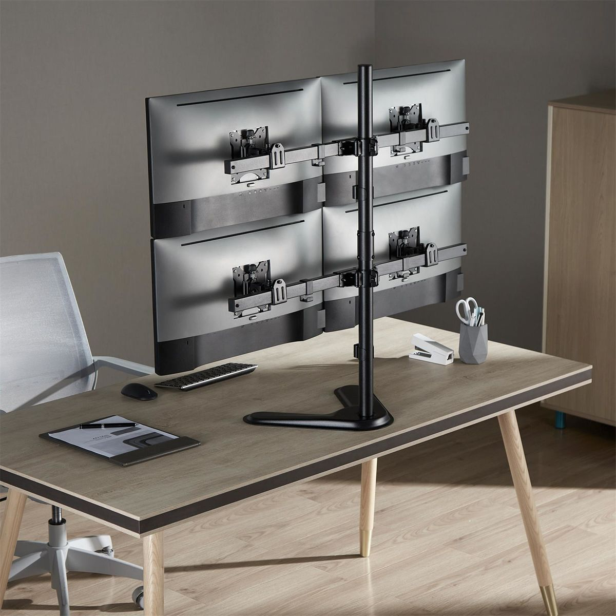 Vier computermonitoren op een standaard op een houten bureau met kantoorbenodigdheden en meubels.