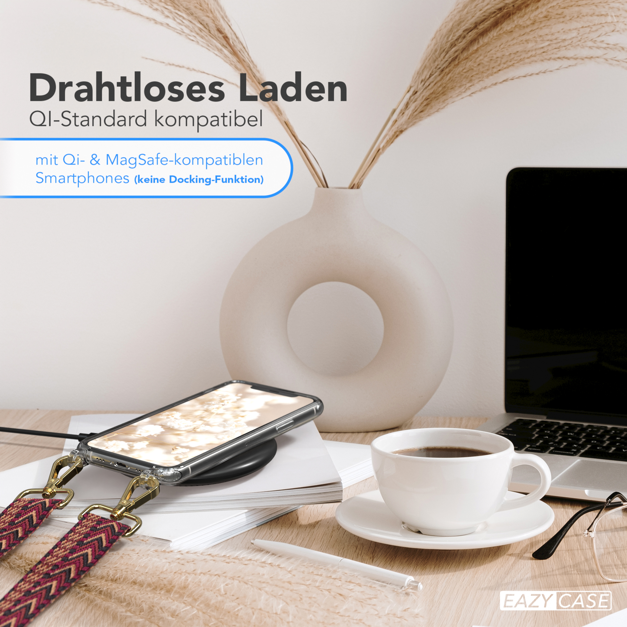 Weiße Vase mit getrockneten Pflanzen, ein Telefon mit Hülle und eine Tasse Kaffee auf einem Schreibtisch.