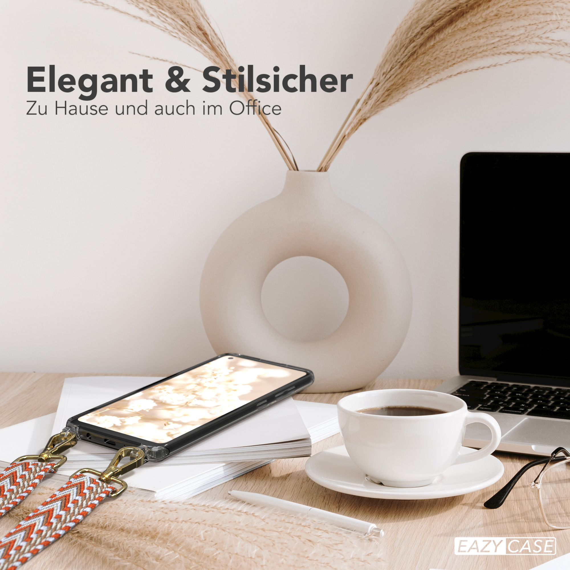 Laptop, Kaffeetasse und Telefon auf einem Schreibtisch. Eine Vase mit Weizen. Die Handyhülle hat einen gemusterten Riemen.