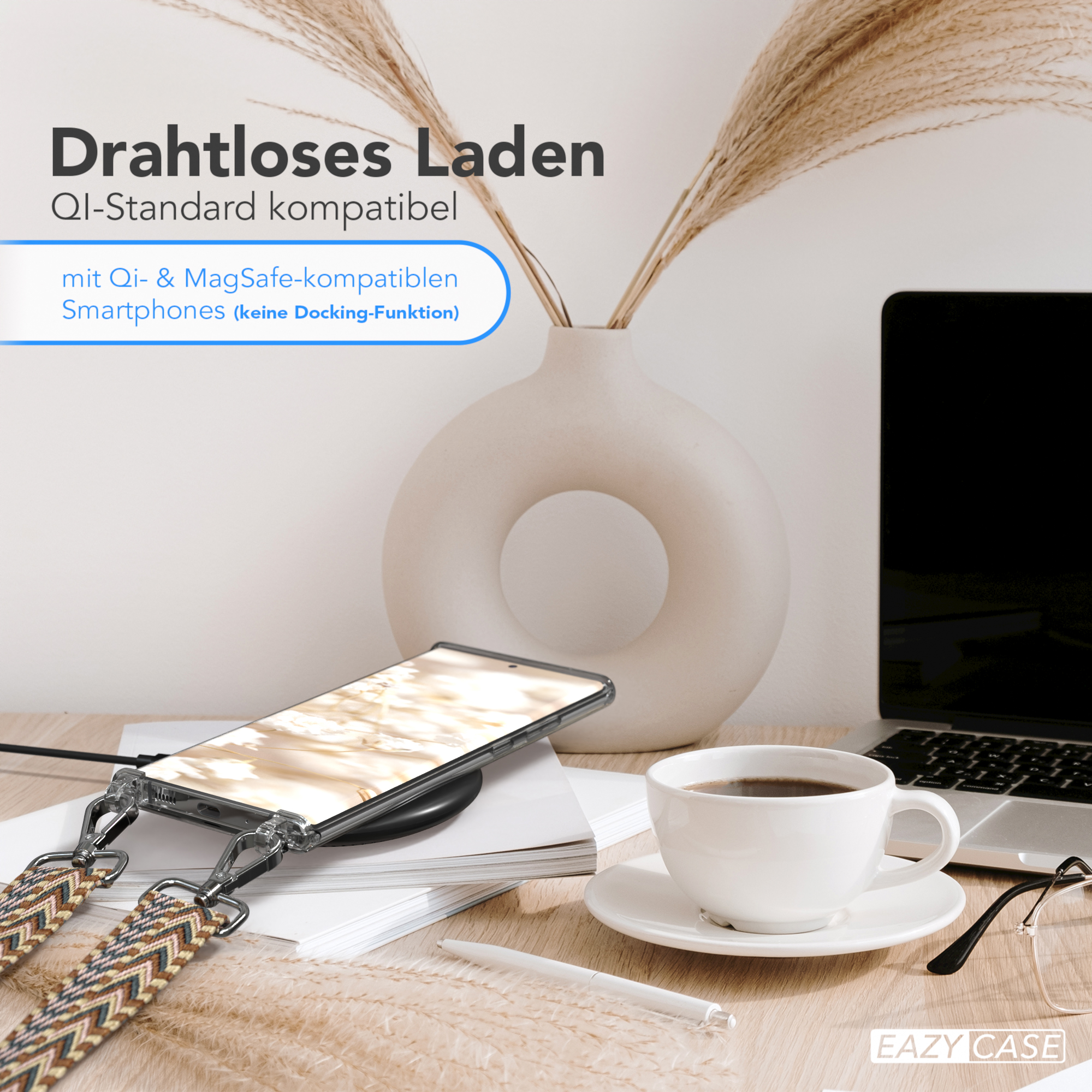 Ein Handy auf einem Ladegerät, eine Tasse Kaffee und ein Laptop auf einem Holztisch.