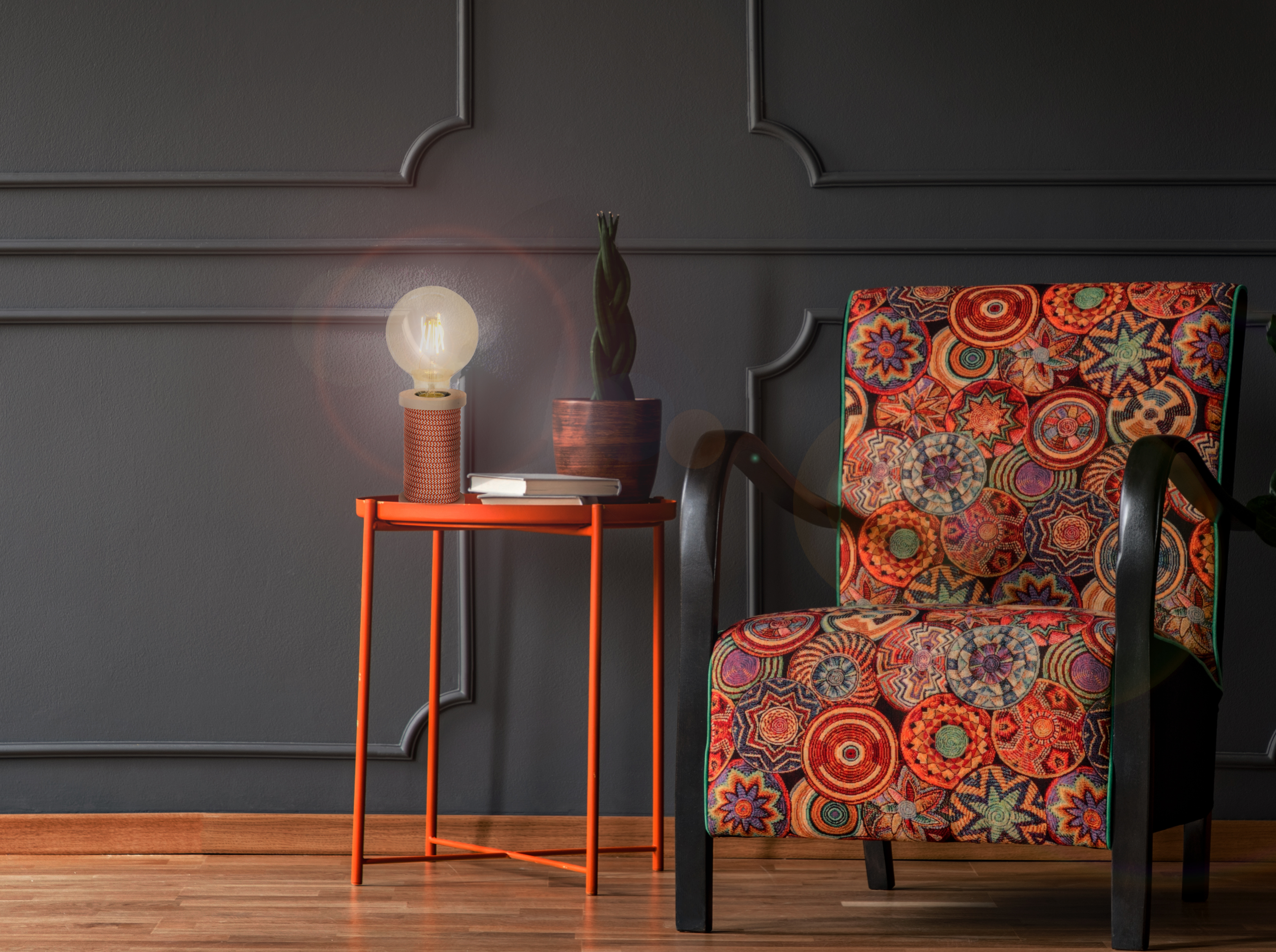 Ein orangefarbener Beistelltisch mit Lampe, Büchern und einer dekorativen Pflanze neben einem gemusterten Stuhl.