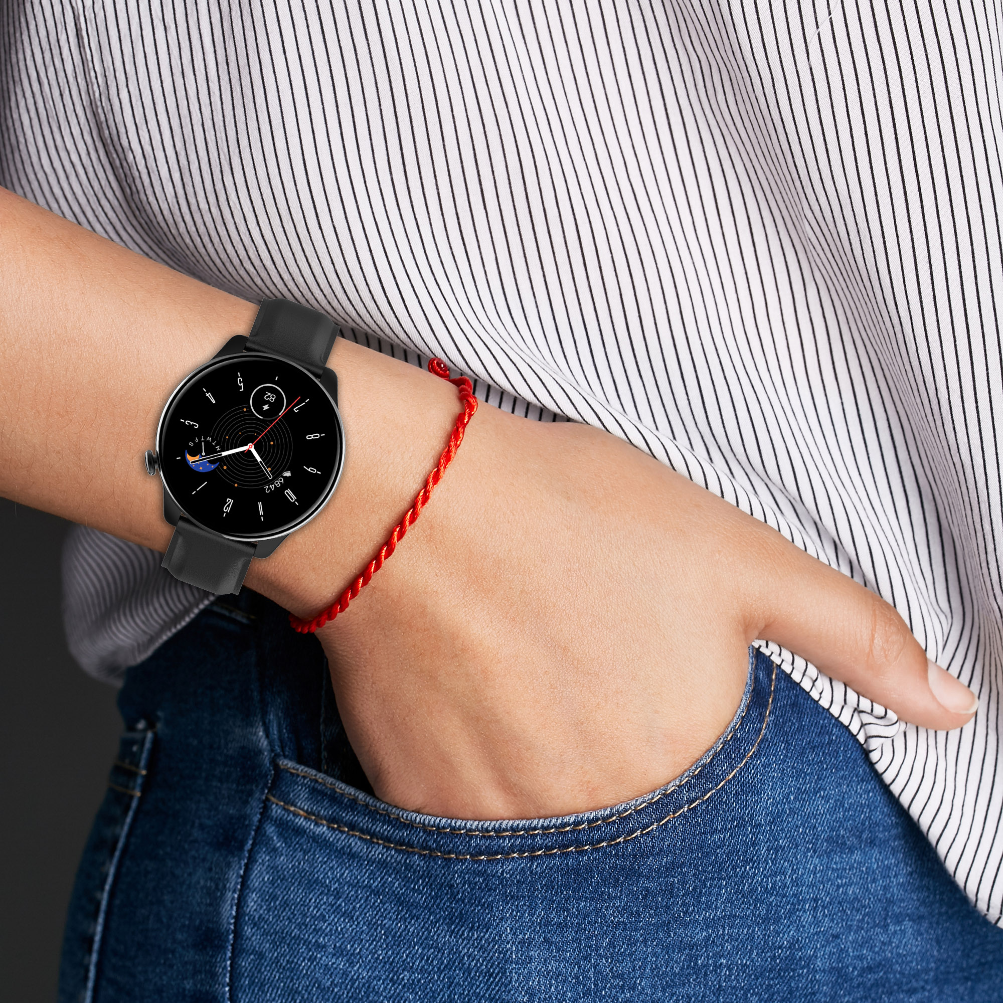 Handgelenk einer Person mit einer schwarzen Smartwatch und einem roten Armband, vor einem gestreiften Hemd.