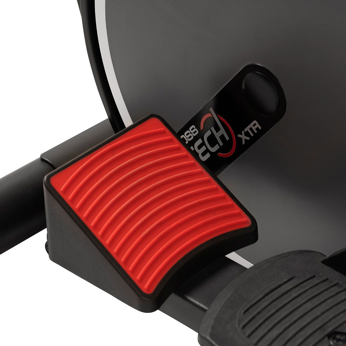 Rotes, geriffeltes Fußpedal mit schwarzem Rahmen und schwarzem Etikett auf einer schwarzen Trainingsmaschine.
