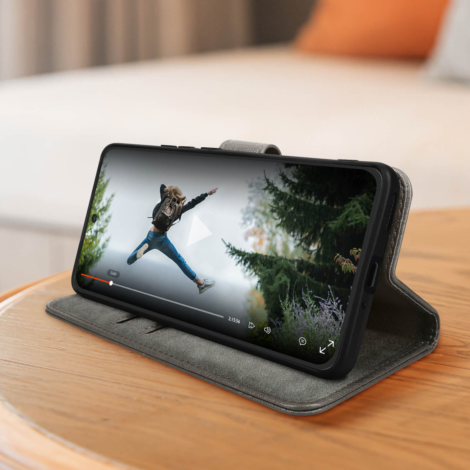Un téléphone dans un étui affiche une vidéo sur une table en bois. L'étui est ouvert et montre une personne sautant.