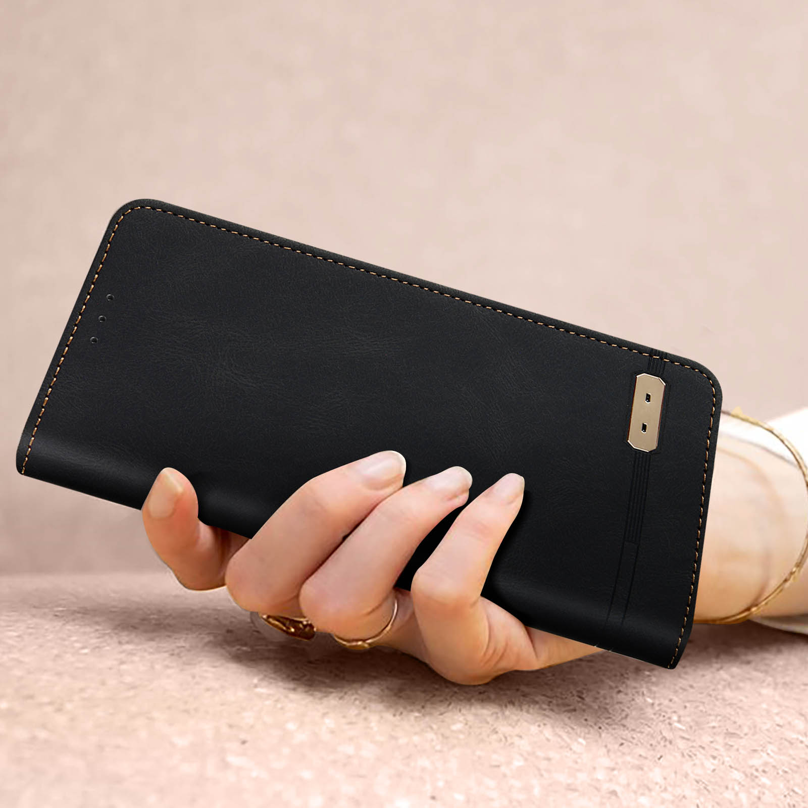 Una custodia per telefono in pelle nera è tenuta in mano. Sono visibili cuciture dorate e un piccolo accento dorato.