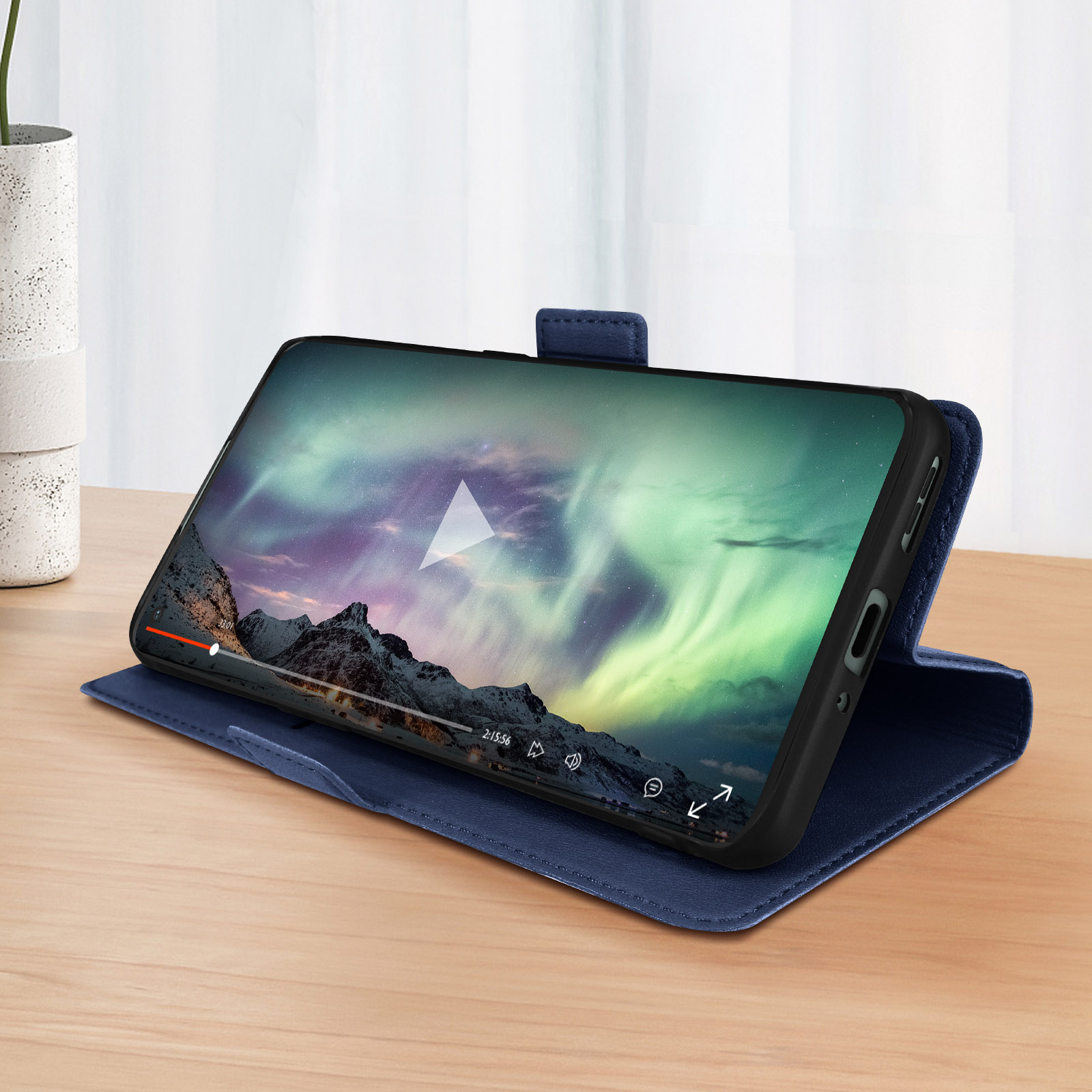 Blaue Handyhülle mit Telefon, das ein Video auf einem Holztisch abspielt. Berge und Aurora im Hintergrund.