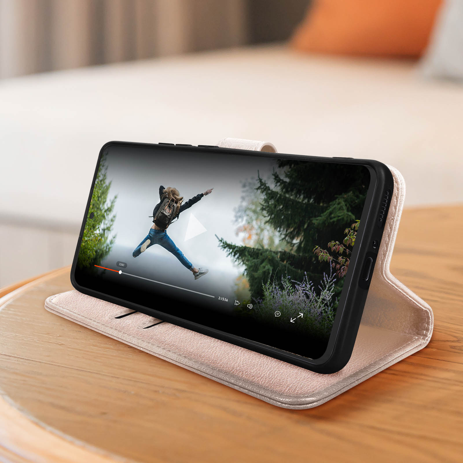 Un téléphone dans un étui affichant une vidéo sur une table en bois. Une femme saute dans la vidéo.