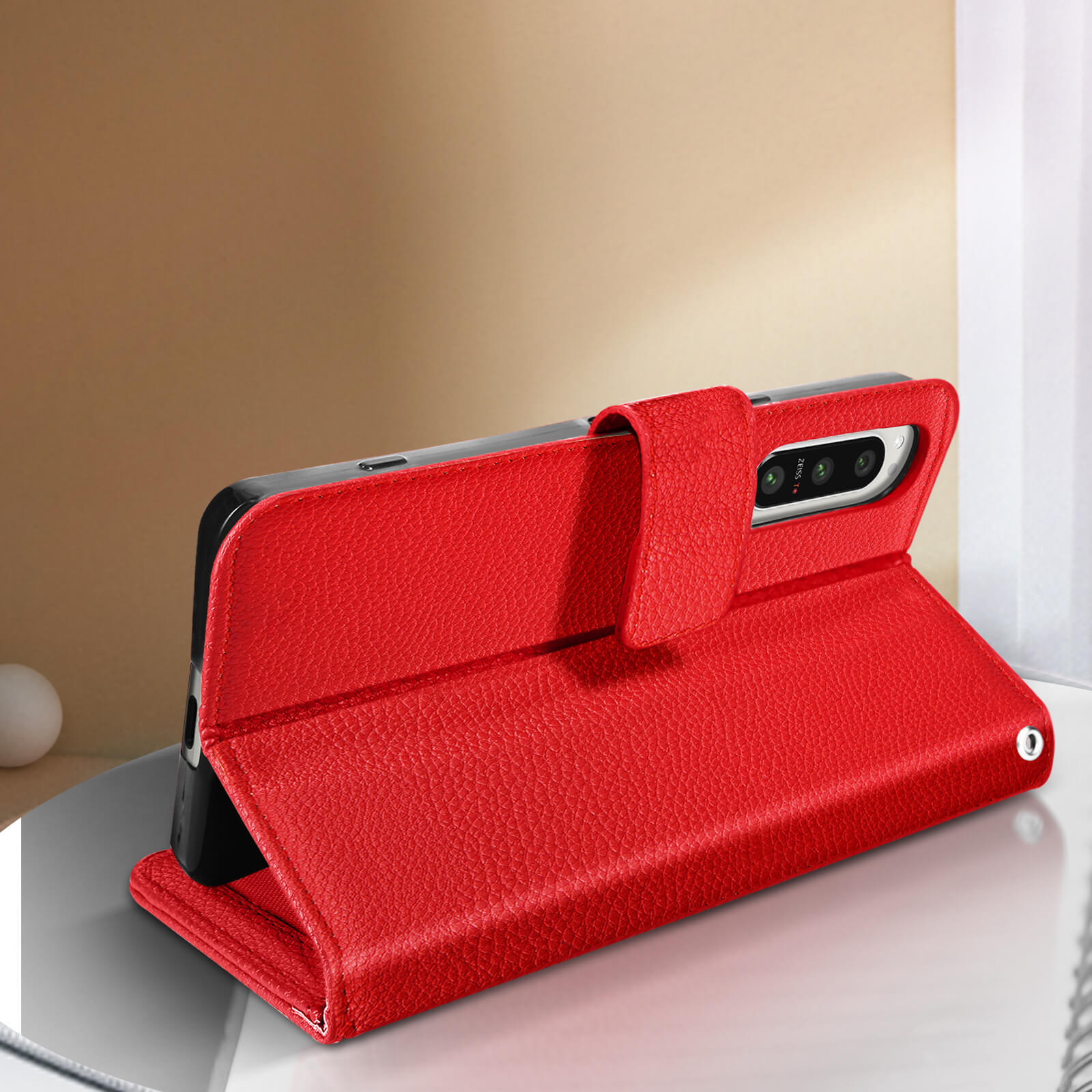 Una funda de teléfono de cuero rojo, abierta, con un teléfono dentro, apoyado en una superficie.
