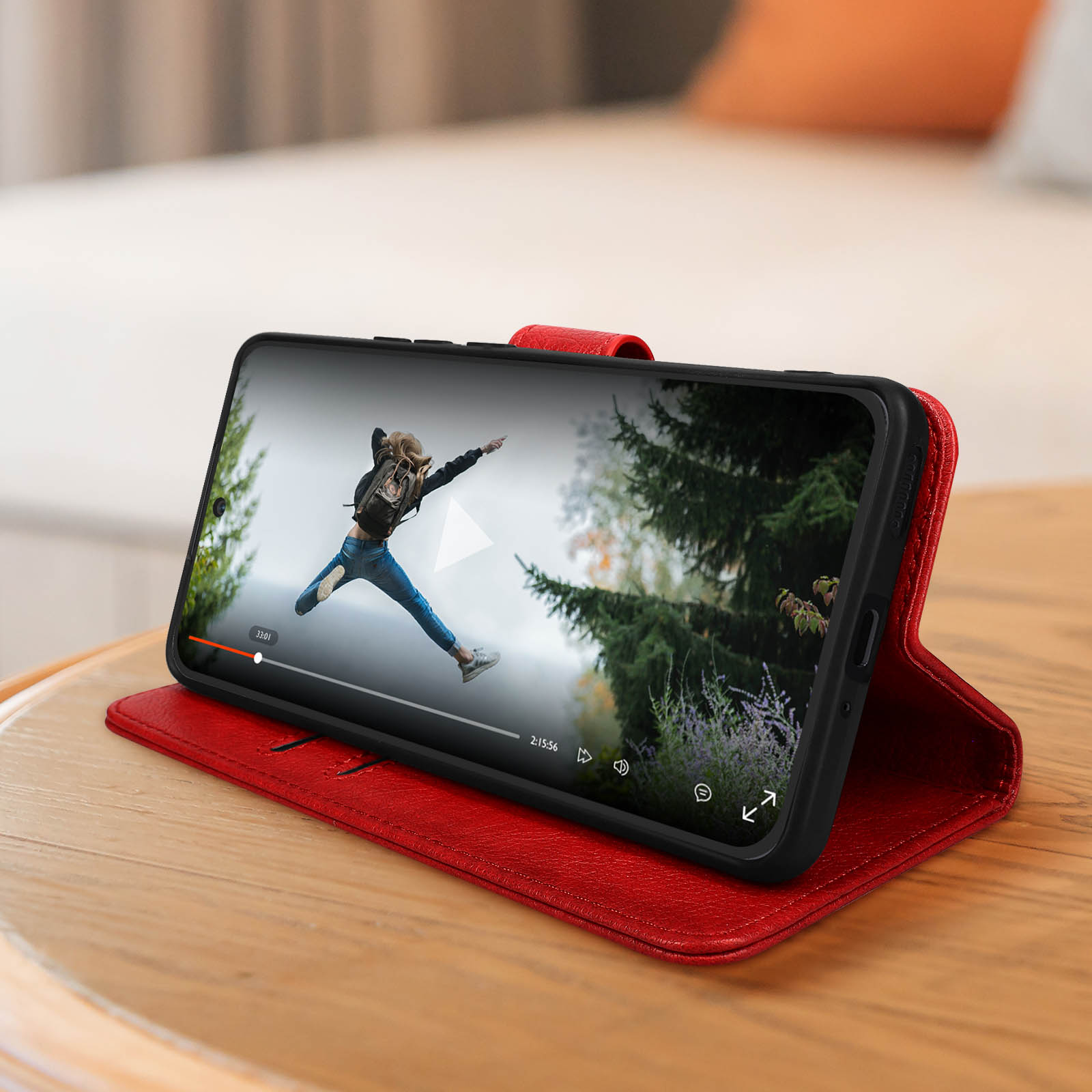 Un téléphone dans un étui rouge affichant une vidéo d'une personne sautant dans une forêt.