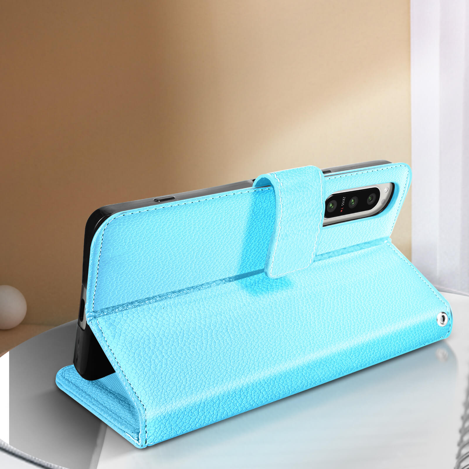 Funda de teléfono de cuero azul claro, abierta, con un teléfono dentro, sobre una superficie reflectante.