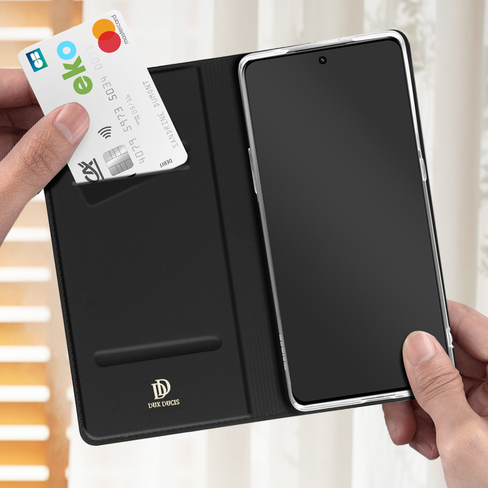 Custodia per telefono nera aperta con un telefono all'interno. Una carta di credito è in uno slot. Una mano tiene la custodia.