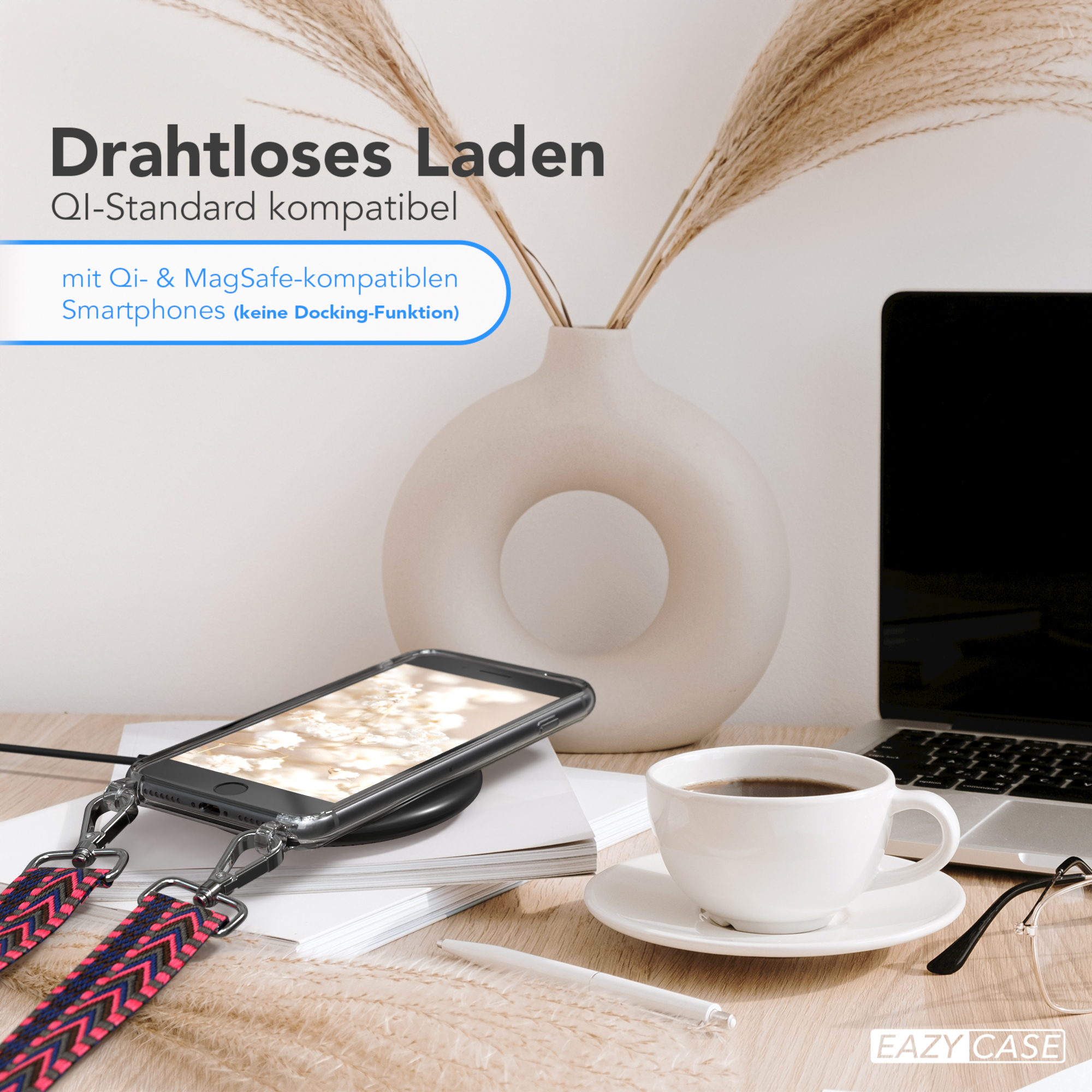 Telefon auf kabellosem Ladegerät mit Kaffeetasse und Vase mit Pampasgras auf einem Schreibtisch. Laptop im Hintergrund.