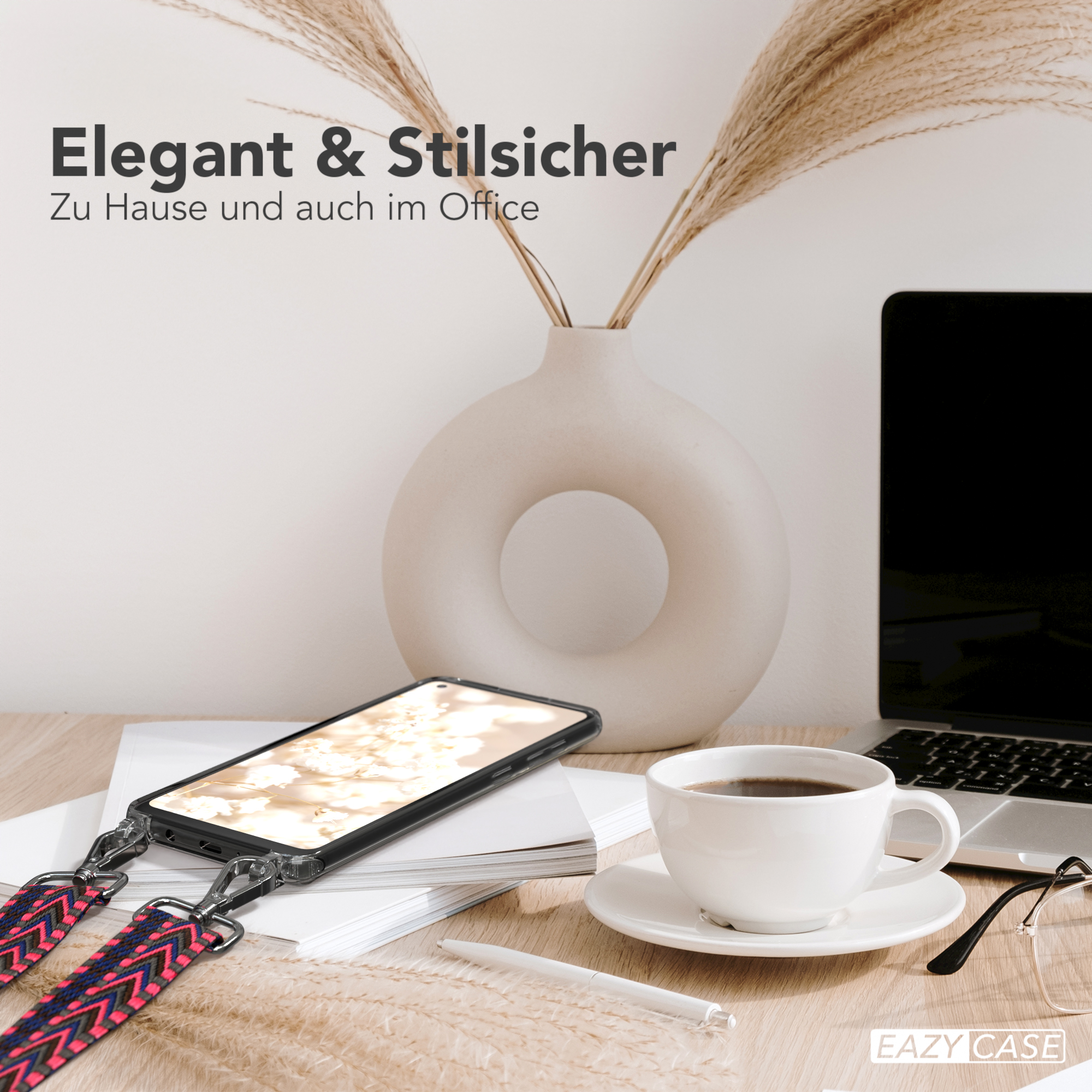 Telefon mit Gurt auf dem Schreibtisch, Kaffee, Blumen und Laptop im Hintergrund.