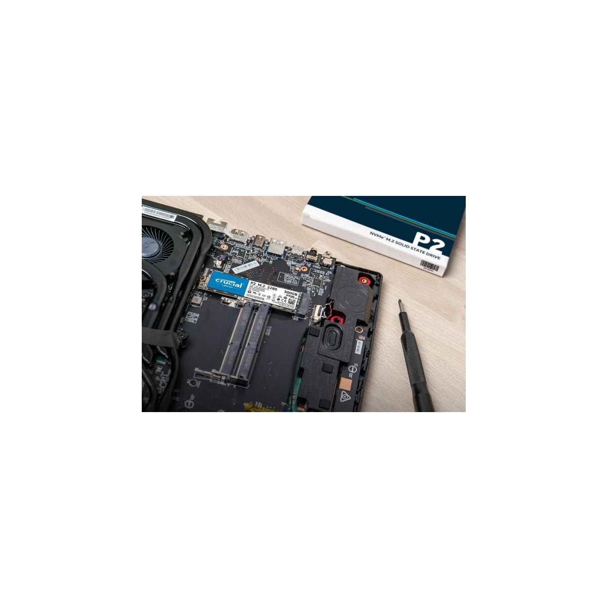Laptop-Innenraum mit installierter SSD, Schraubendreher und einer Box auf Holz.