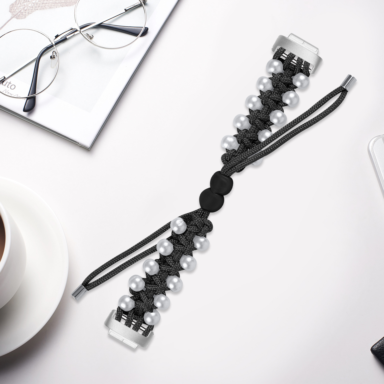 Schwarzes Armband mit weißen Perlen. Es liegt auf einer weißen Oberfläche mit Brille und Tasse.