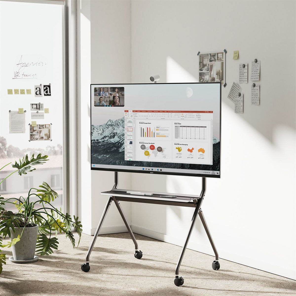 Een groot scherm op een rolstandaard toont een videoconferentie, met documenten en grafieken.