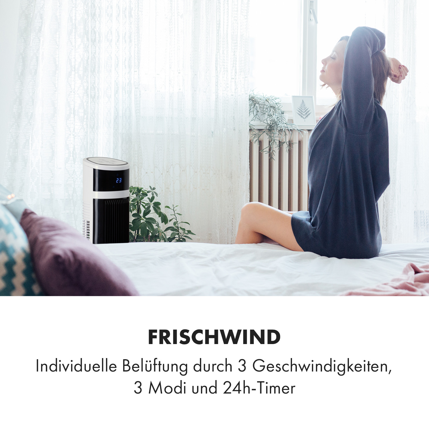 Eine Frau sitzt auf einem Bett mit einem weißen Luftreiniger daneben.
