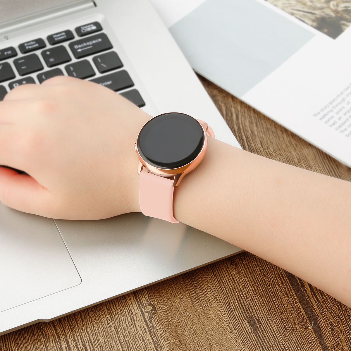 Das Handgelenk einer Person mit einer roségoldenen Smartwatch. Die Uhr hat einen schwarzen Bildschirm und ein pinkes Armband.
