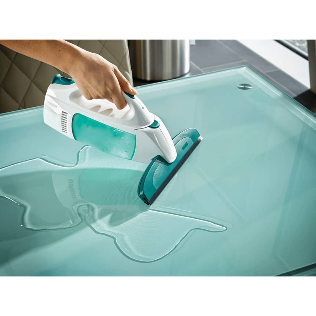 Osoba czyszcząca szklany stół za pomocą ręcznego narzędzia czyszczącego. Na stole jest woda.