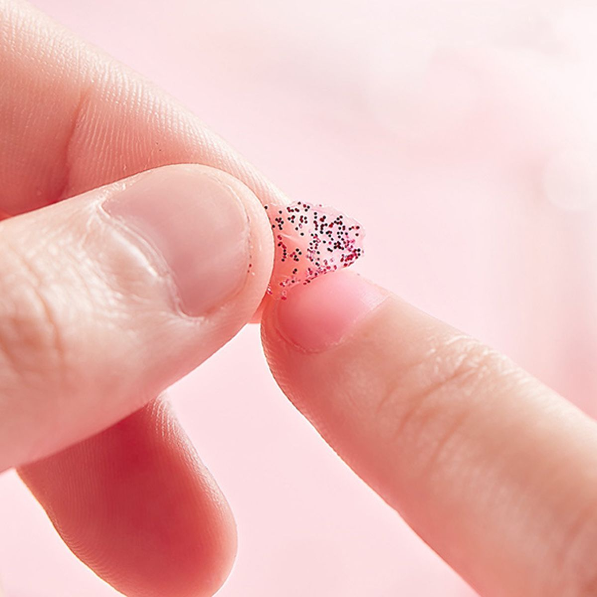 Finger halten ein kleines, rosa, glitzerndes Objekt.