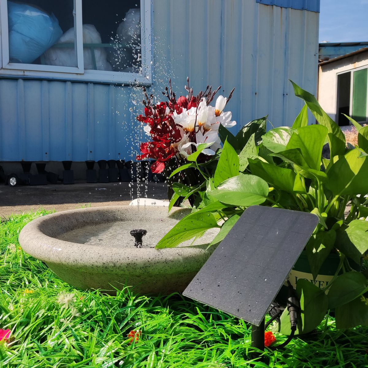 Ein kleiner Springbrunnen mit Blumen und einem Solarpanel in einem Garten.