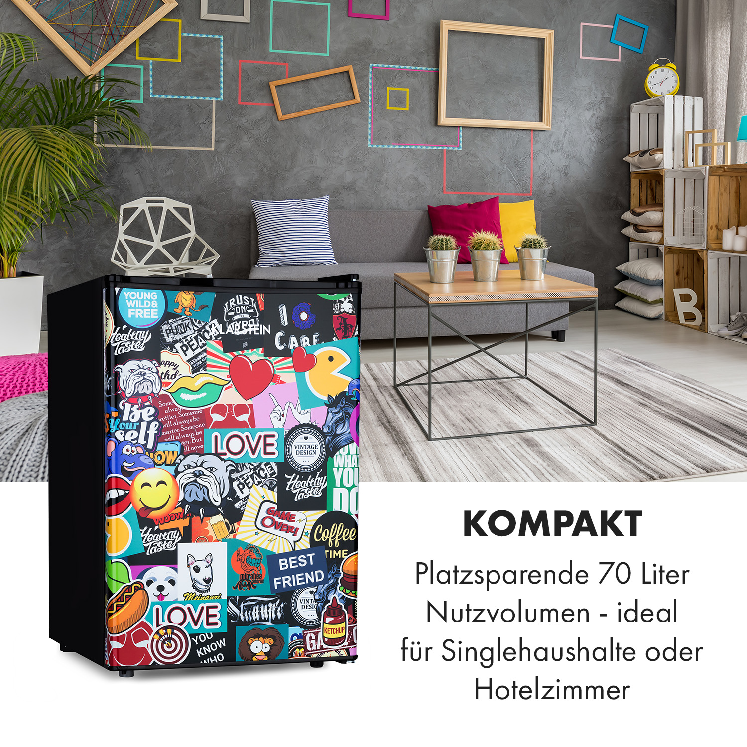 Kleiner Kühlschrank mit Aufklebern, mit einer grauen Couch, gerahmten Bildern und Pflanzen im Hintergrund.