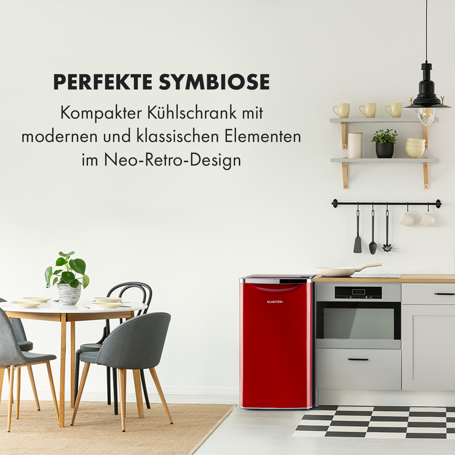 Ein roter Mini-Kühlschrank steht in einer Küche. Im Vordergrund stehen ein Tisch und Stühle. Ein Fenster und Regale sind sichtbar.
