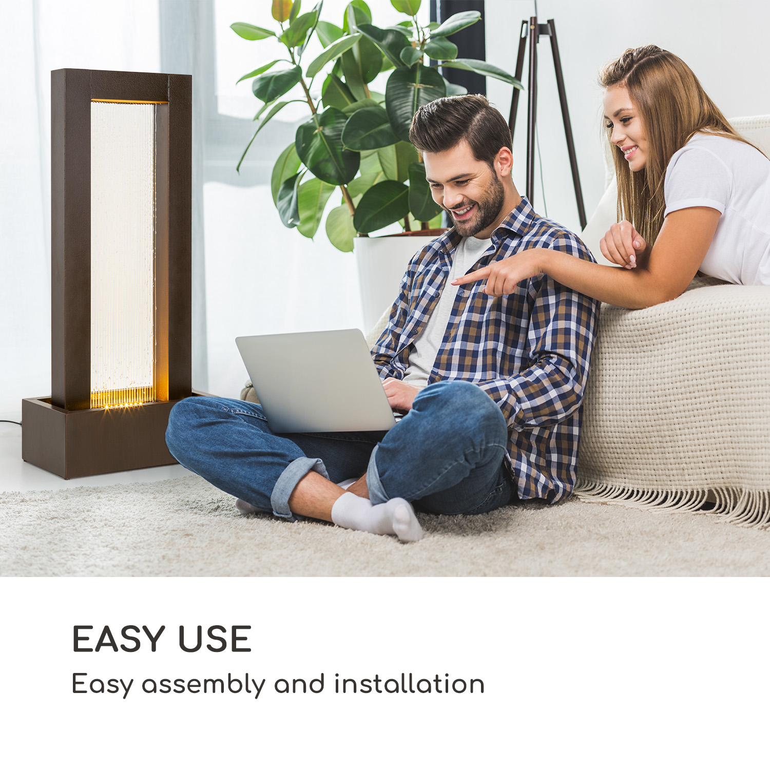 Ein Paar schaut sich einen Laptop auf dem Boden an. Eine dekorative Lampe ist im Hintergrund.