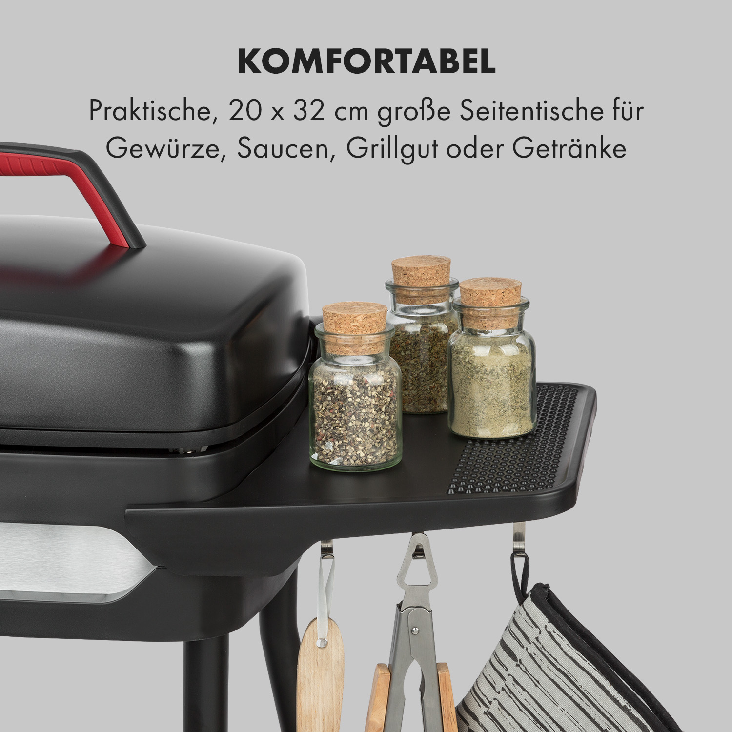 Ein schwarzer Grill mit Gewürzen. Gewürze in Gläsern und Utensilien unter dem Beistelltisch.
