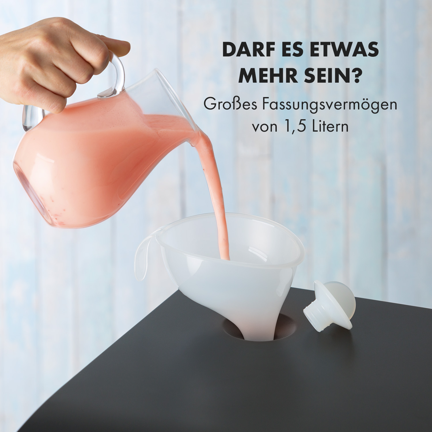 Eine Hand gießt rosa Flüssigkeit aus einem Glaskrug in einen weißen Trichter auf eine dunkelgraue Oberfläche.