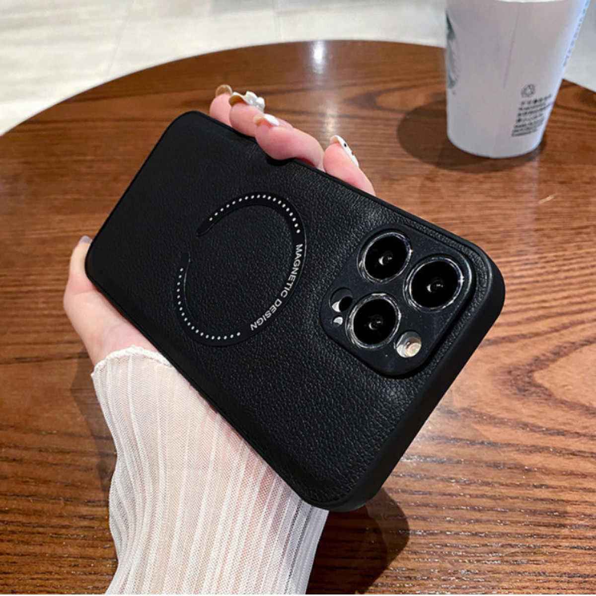 Schwarze Handyhülle mit Magnetdesign auf Holztisch, gehalten von Hand.