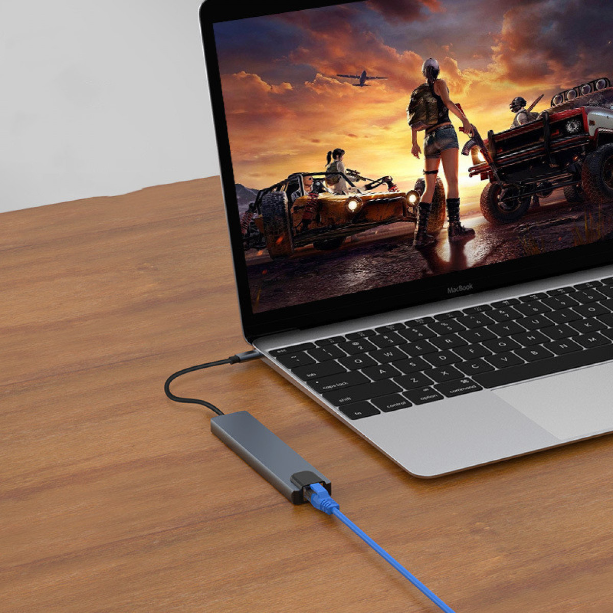 Laptop jest podłączony do koncentratora za pomocą niebieskiego kabla sieciowego. Laptop pokazuje scenę z gry wideo.