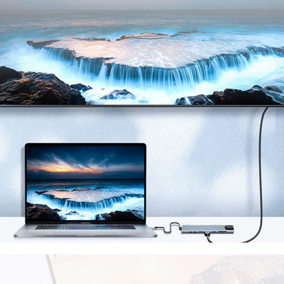 Laptop podłączony do huba, z telewizorem pokazującym krajobraz morski w tle.